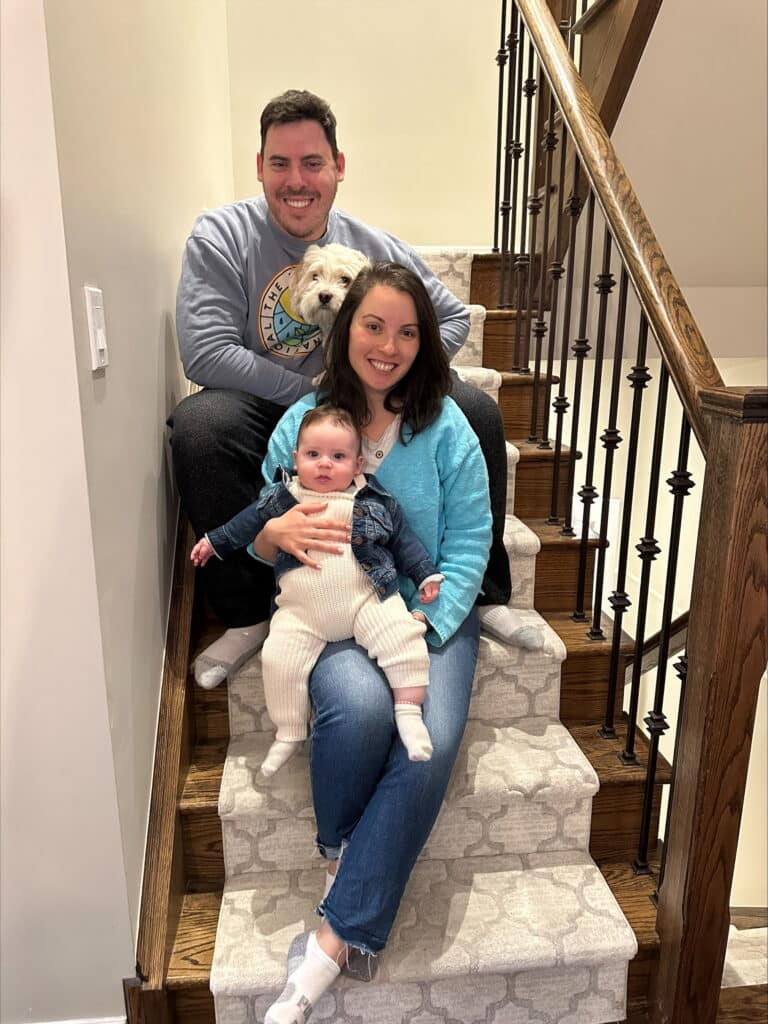 Equivant's Director of Customer Success, Danna Levine-Poch, sits on the steps holding her son with her husband and dog sitting behind her.